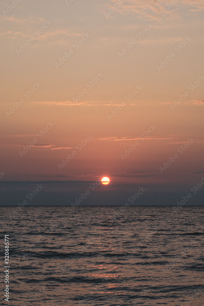 Red soft frosted sunset over the sea. Red disk of the sun