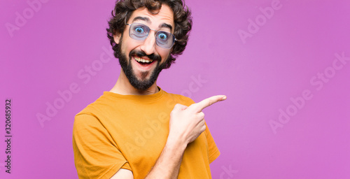 young crazy cool man looking excited and surprised pointing to the side and upwards to copy space against flat wall