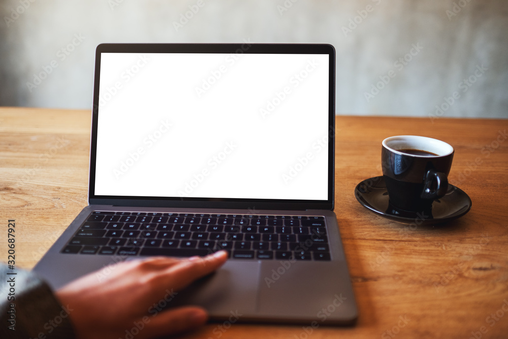 Mockup image of a woman using and touching on laptop touchpad with blank white desktop screen with coffee cup on the table Mockup image of a woman using and touching on laptop touchpad with blank white desktop screen with coffee cup on the table