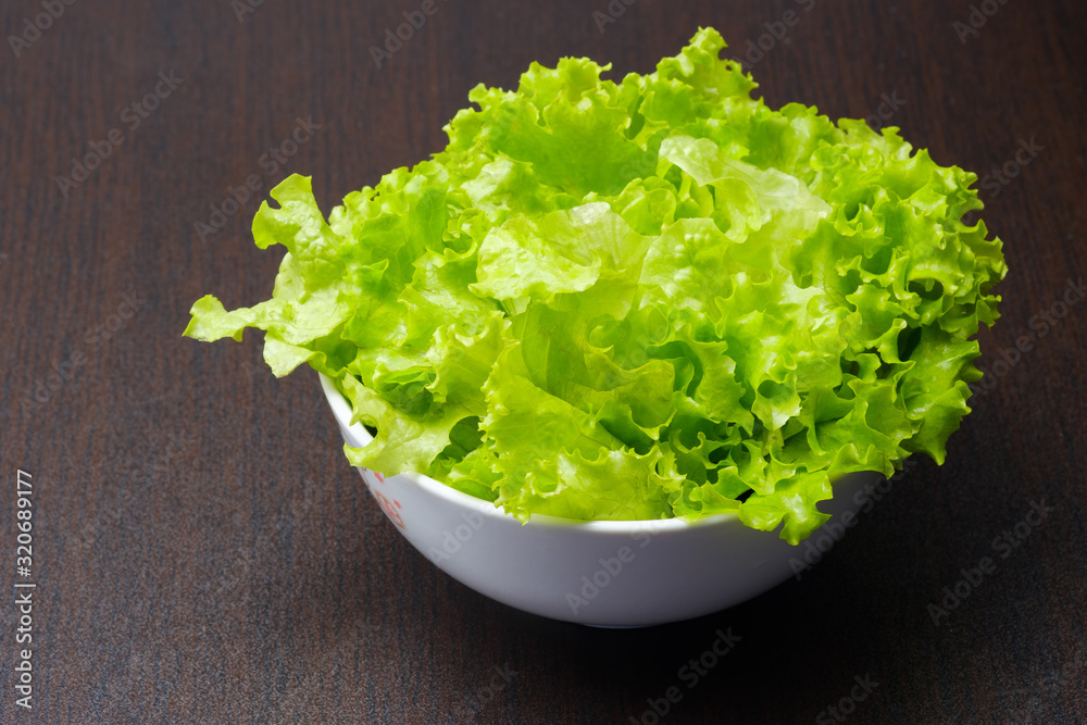 Green lettuce in white bowl on wooden background Green lettuce in white bowl on wooden background