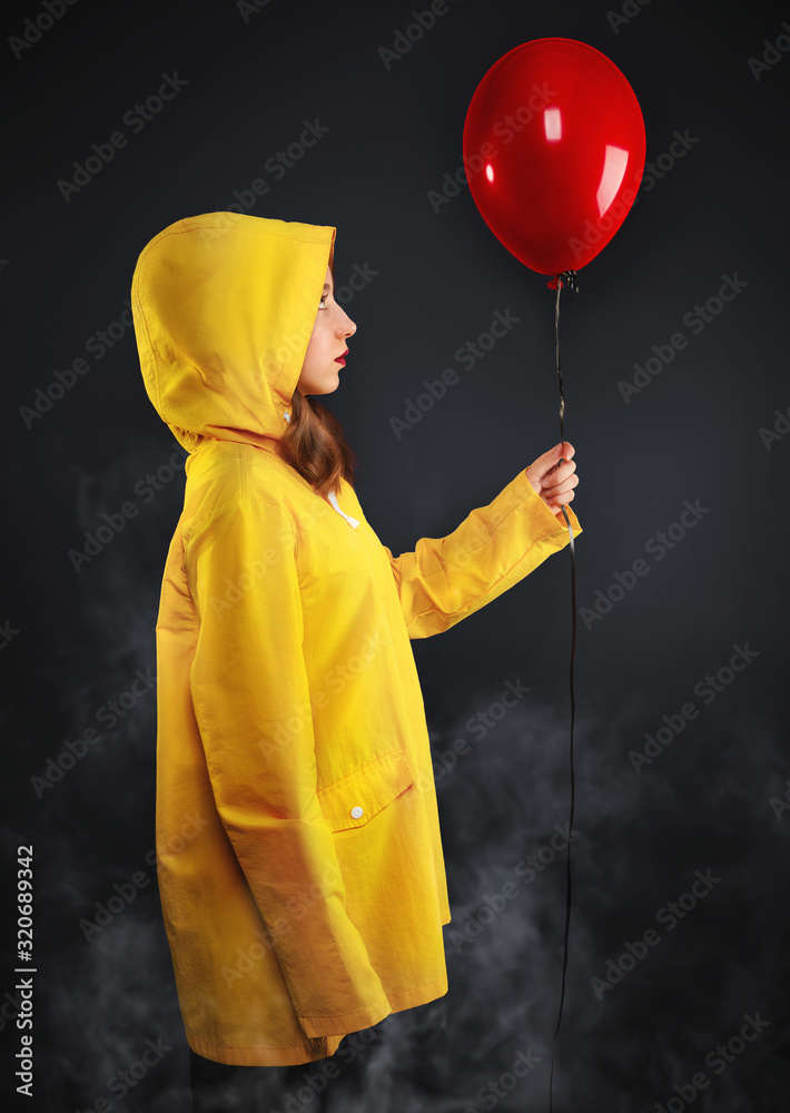 Sad little girl in haze in yellow coat with hood hold red air balloon ...