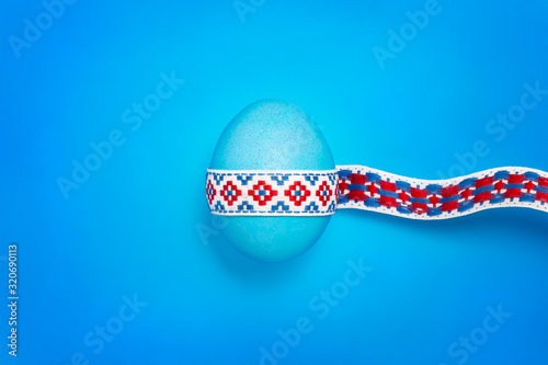 Blue shine egg with a national traditional ribbon on a blue background