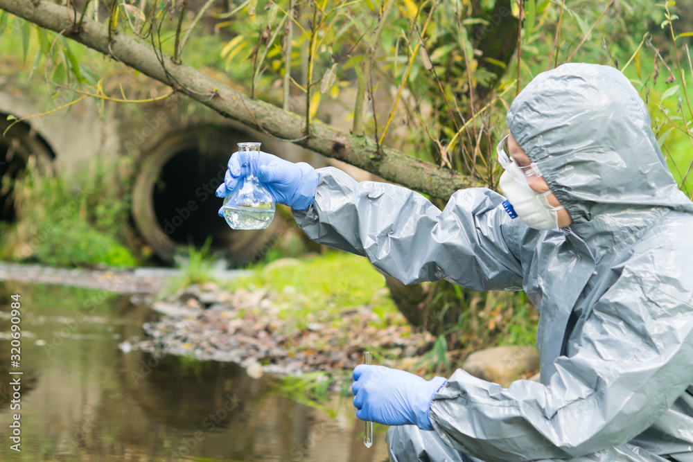 environmental biologist in a protective suit and mask examines water from the river for viruses environmental biologist in a protective suit and mask examines water from the river for viruses