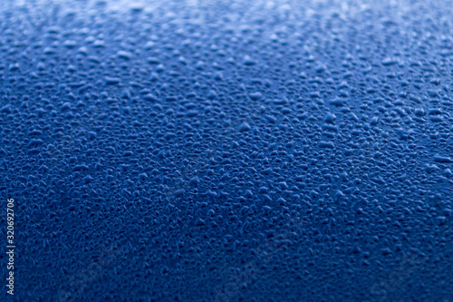Rain drop on dark blue surface. Spring morning mood. Bright background or wallpaper. Texture of water droplets.