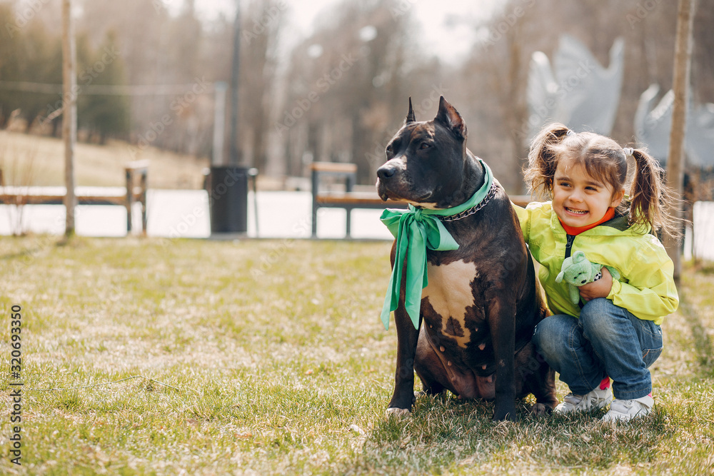 Beautiful little girl in a green jacket. Child in a summer park with a dog