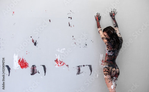 Obraz na plátně Woman in underwear, sportswear, young and sexy, artistically abstract painted with black, red, white, paint, rolls off in front of wall in studio and leaves colorful color prints, copy space
