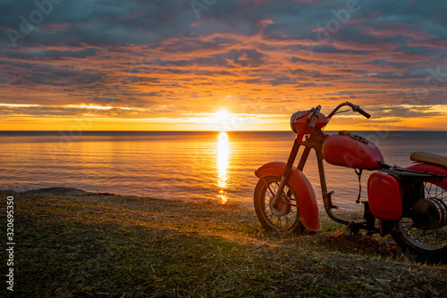 A skeleton of an old red motorcycle against the picturesque sunrise.