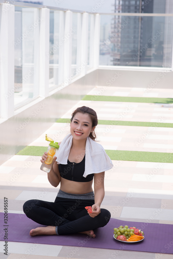 Young woman in stylish sportswear sitting and relaxing on the floor with plastic bottle of water after workout on the rooftop. Young woman in stylish sportswear sitting and relaxing on the floor with plastic bottle of water after workout on the rooftop.