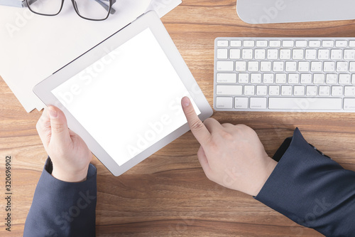 Businessman using tablet over the wooden desk with computer and office supplies in modern work space, pointing finger at blank screen for adding your content. Business and technology concept. Top view