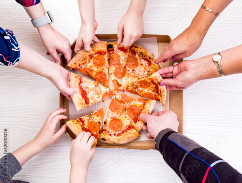 Everyone loves pizza. Close-up top view of young people choosing slices of pizza during lunch indoors.