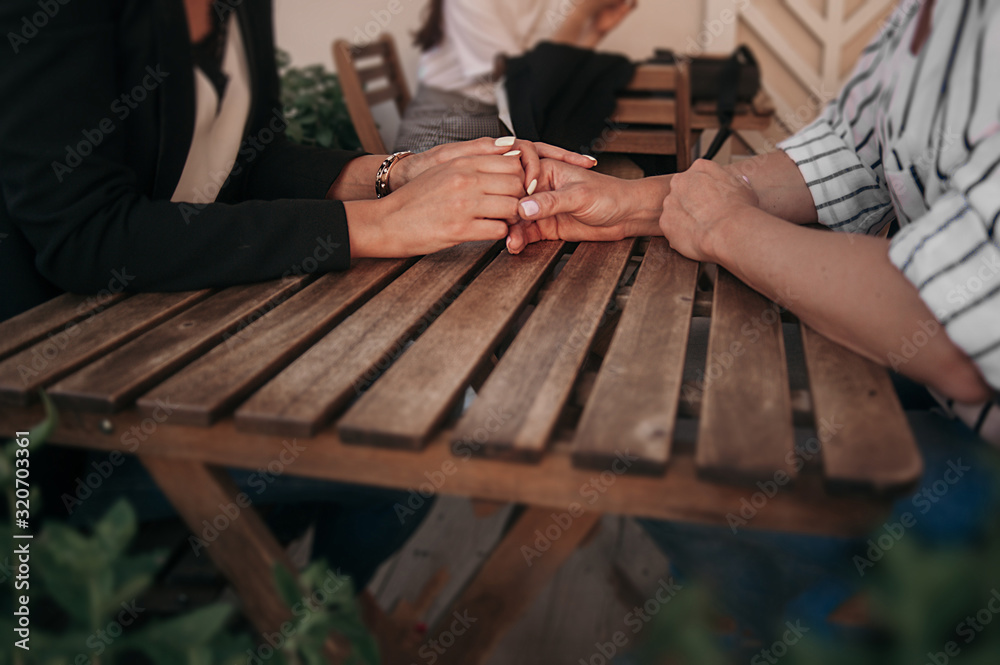 women without faces tenderly hold each other's hands at a wooden table in a street cafe, open female relationships in public women without faces tenderly hold each other's hands at a wooden table in a street cafe, open female relationships in public