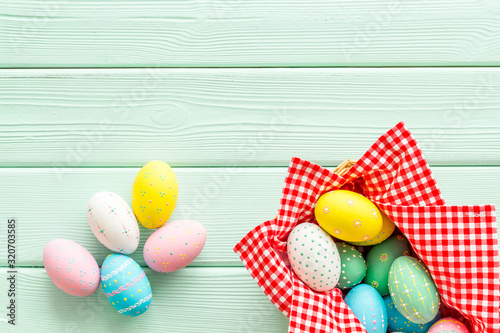 Easter eggs painted in basket on green wooden desk top-down copy space