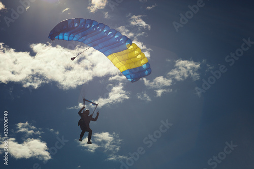 Skydiver under the canopy of a parachute, lit by bright sunlight, close-up.