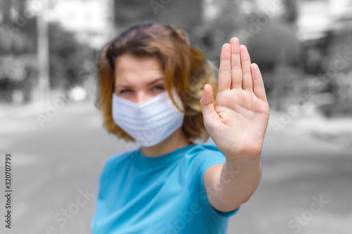 Girl, young woman in protective sterile medical mask on her face outdoors, on asian street show palm, hand, stop no sign. Air pollution, virus, Chinese pandemic coronavirus concept. Focus on hand.