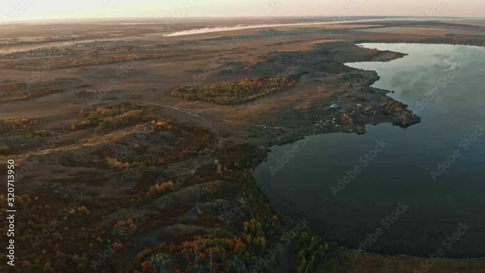 Bird eye view of valley, forests, fields and lake illuminated by setting sun. Yellow, orange and red autumn trees, country roads, small settlements on shore, aerial drone landscape Bird eye view of valley, forests, fields and lake illuminated by setting sun. Yellow, orange and red autumn trees, country roads, small settlements on shore, aerial drone landscape
