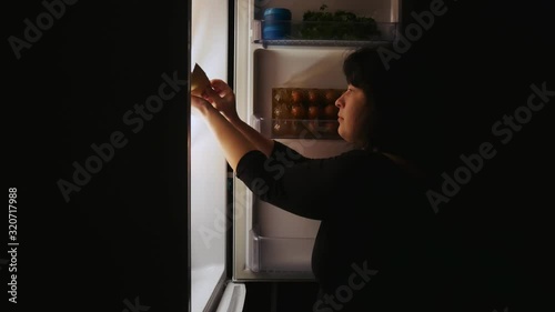 Fat woman opens the fridge at night and takes the cake.Hunger,overeating,diet.