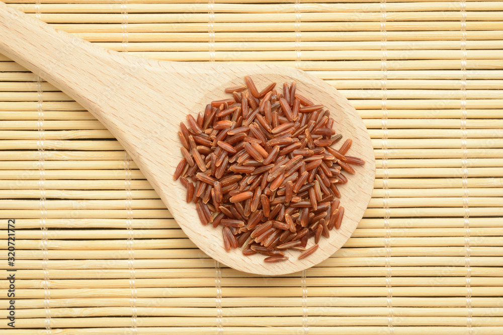 Arroz rojo integral crudo en una cuchara de madera Arroz rojo integral crudo en una cuchara de madera