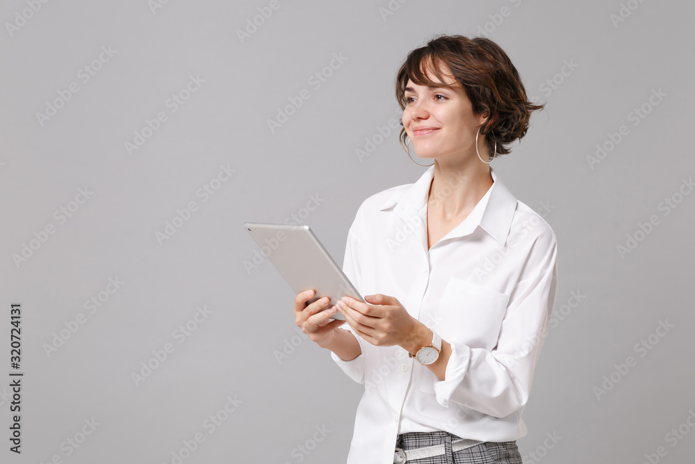 Pretty young business woman in white shirt posing isolated on grey wall background studio portrait. Achievement career wealth business concept. Mock up copy space. Holding, using tablet pc computer. Pretty young business woman in white shirt posing isolated on grey wall background studio portrait. Achievement career wealth business concept. Mock up copy space. Holding, using tablet pc computer.