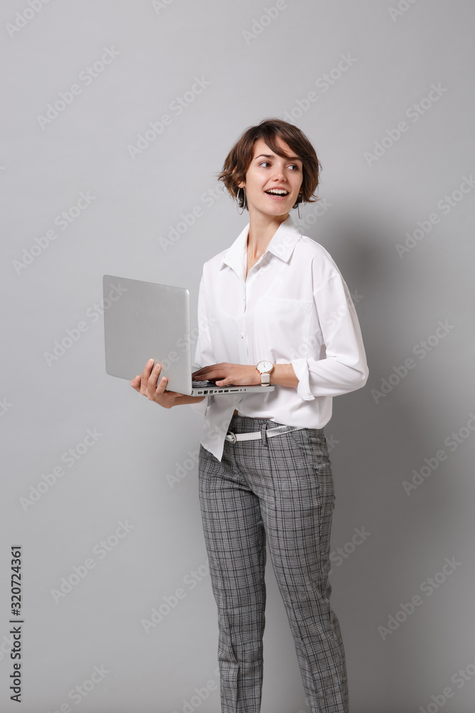 Beautiful young business woman in white shirt posing isolated on grey wall background. Achievement career wealth business concept. Mock up copy space. Working on laptop pc computer, looking aside. Beautiful young business woman in white shirt posing isolated on grey wall background. Achievement career wealth business concept. Mock up copy space. Working on laptop pc computer, looking aside.