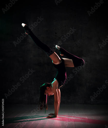 Teenage gymnast in black leotard, knee socks and ballet shoes, performing exercises standing on her hands, upside down. Close-up