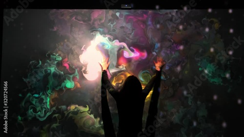 Girl plays with an interactive video installation. New art form, generative graphics. Silhouette of girl draws multi-colored paints interactive installation. photo