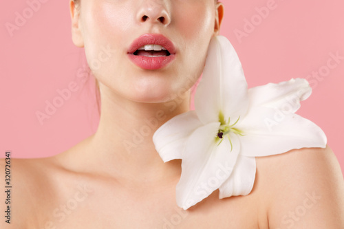 Close up cropped blonde half naked woman 20s perfect skin nude make up isolated on pastel pink wall background studio portrait. Skin care healthcare cosmetic procedures concept. Mock up lily flower.