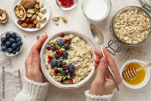 healthy breakfast. Woman eating oatmeal porridge with fresh berry, nuts and honey photo
