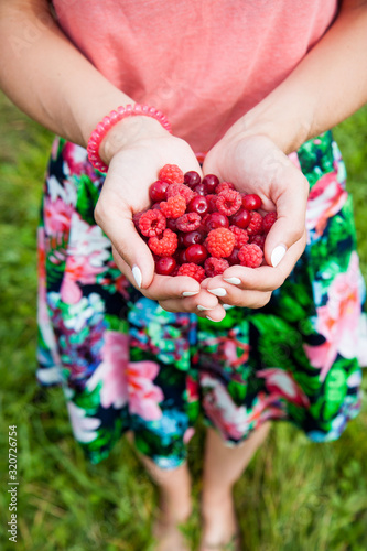 Young woman's hands holding a handful of red berries, cherries, raspberries and red currant. 