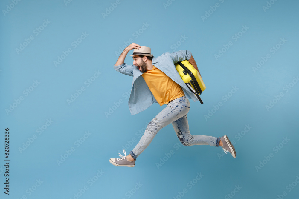 Side view of excited traveler tourist man in yellow clothes isolated on blue background. Male passenger traveling abroad on weekends. Air flight journey concept. Jumping like running, hold suitcase. Side view of excited traveler tourist man in yellow clothes isolated on blue background. Male passenger traveling abroad on weekends. Air flight journey concept. Jumping like running, hold suitcase.