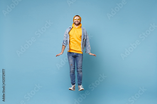 Smiling young hipster guy in fashion jeans denim clothes posing isolated on pastel blue background studio portrait. People sincere emotions lifestyle concept. Mock up copy space. Jumping, having fun.
