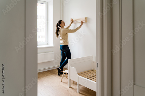 Young woman renovation child room in new house. Wooden bookshelf. Neutral nursery