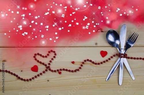 Valentine concept. Fork, knife and tablespoon tied with red pearls. Pink smoke with magic light.Invitation to the Valentine`s menu. Spoon, fork, knife, red pearls, hearts and pink smoke.