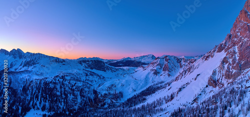 Aerial, colorful panoramic winter view on Pale di San Martino mountains covered in snow. Passo Rolle view, evening mountainscape, orange and dark blue sky. Dolomites, San Martino di Castrozza, Italy. photo