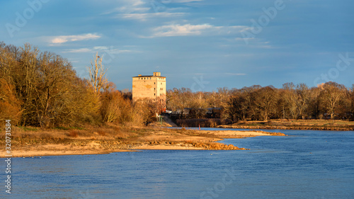 Wallpaper Mural Germany, Saxony-Anhalt, Dessau-Rosslau: Elbe river in late afternoon sun light with abondoned tower, trees, calm floating water and blue sky in background - concept public park nature riverbank. Torontodigital.ca