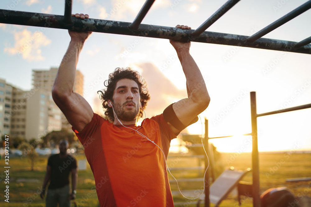 Portrait of a young crossfit sportsman exercising on bar, doing pull-ups for arms and back muscles at the outdoor gym park - obrazy, fototapety, plakaty 