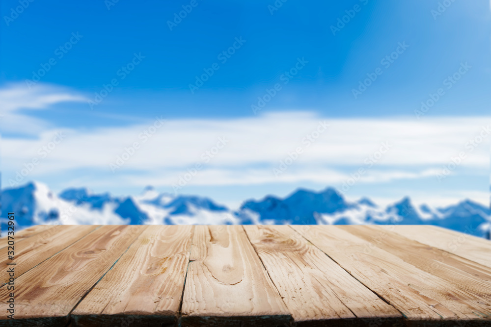Empty wooden surface on blurry background of snowy mountainous area on winter day and blue sky.