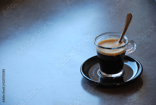 A small cup of espresso black coffee with a teaspoon on a neutral grey background