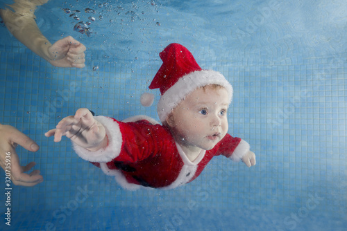 Little baby girl red New Year's dress swims underwater in a swimming pool