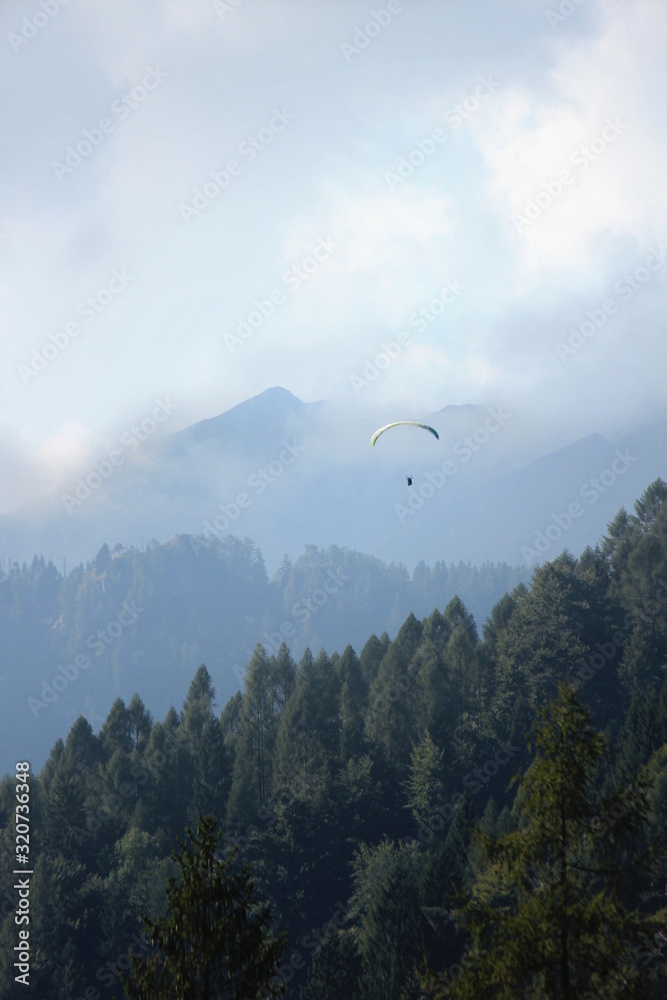 Parapendista in volo co sfondo di montagne e nuvole
