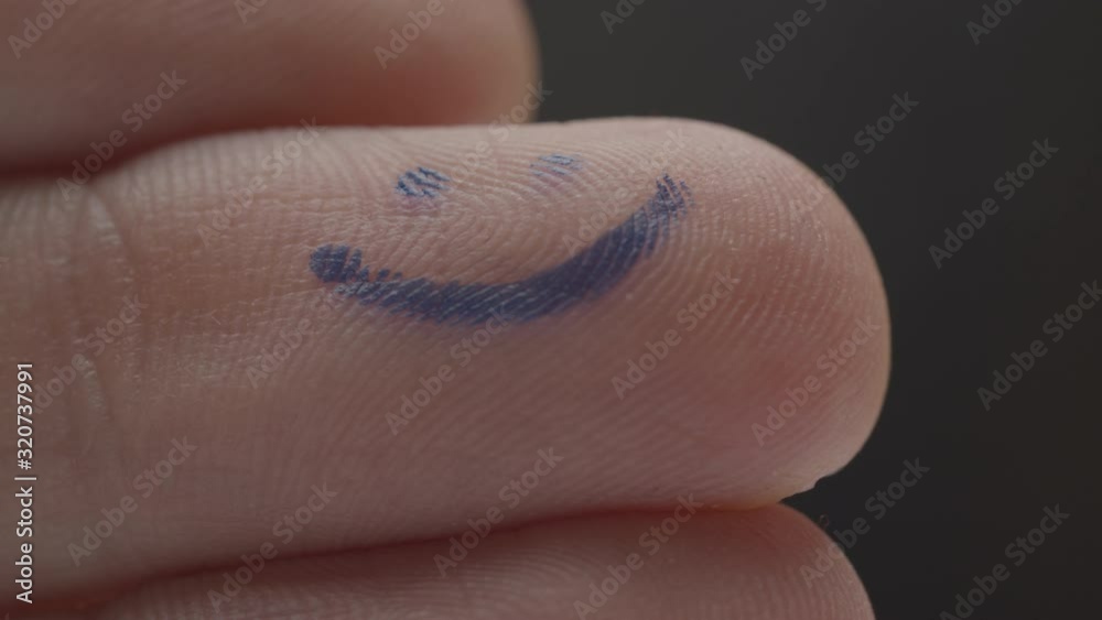 Writing blue happy smiley on finger pad, macro view. Hand with blue ...
