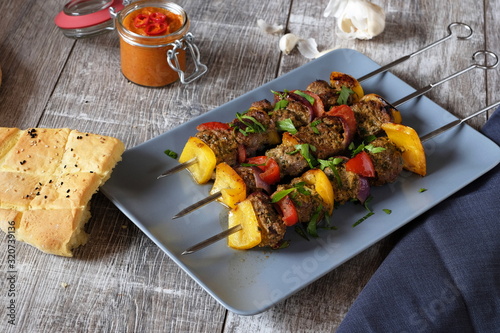 drei spieße Schisch Kebab mit Lammfleisch Paprika und Zwiebeln auf grauem teller und Holztisch Pitabrot ajvar und knoblauch im Hintergrund  photo