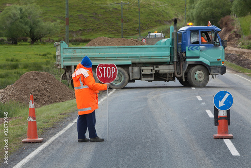Man with stop sign at roadworks. Flagman. Traffic warden. Truck turning. New Zealand