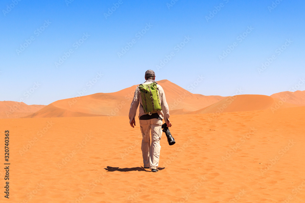 Carta da parati Man with backpack and big camera walking on the red sand dunes of Sossusvlei, Na