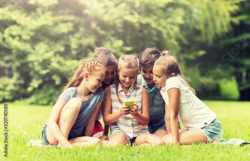 friendship, childhood, technology and people concept - group of happy kids or friends with smartphone in summer park