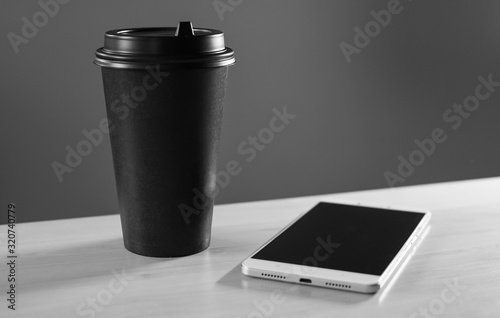 Coffee and smartphone. A cup of coffee on the table. The smartphone lies on the table next to a cup of coffee. Coffee and news. Breakfast.