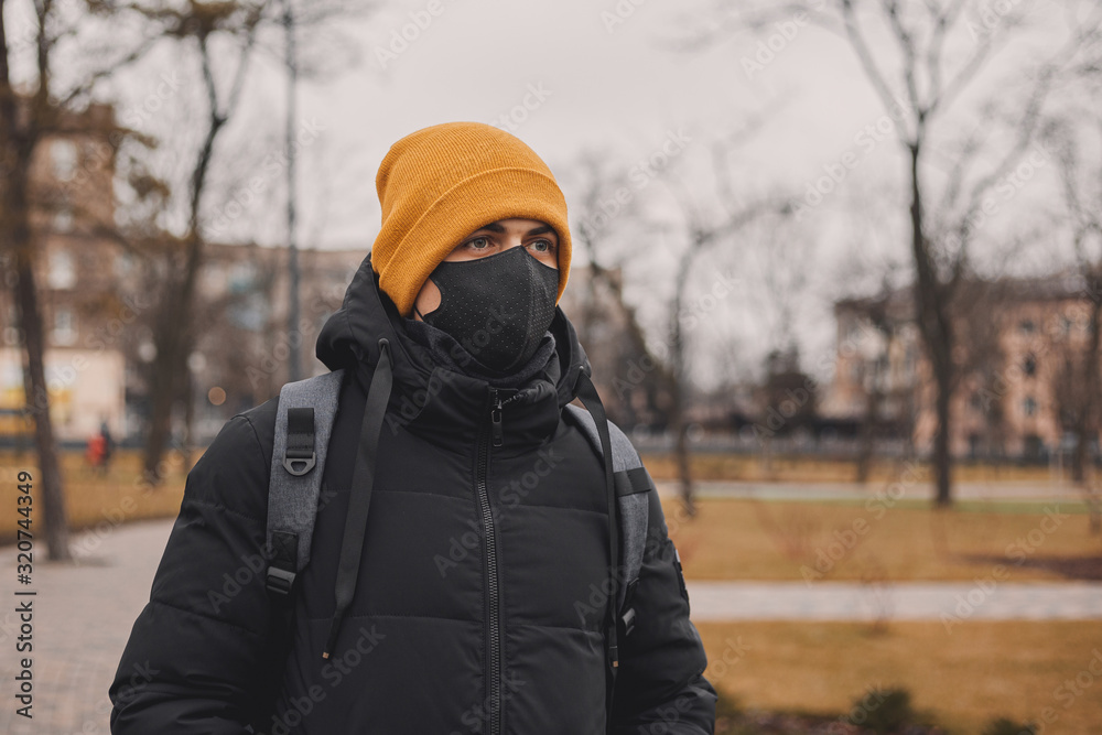 Man in orange hat and black medical mask on the street. Coronavirus is a virus that is endemic in China. Protection from the illness for children. Health safety concept. Man in orange hat and black medical mask on the street. Coronavirus is a virus that is endemic in China. Protection from the illness for children. Health safety concept.
