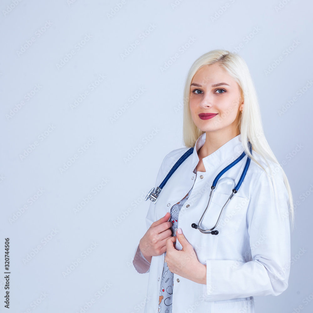 Medical concept of beautiful female doctor in white coat with phonendoscope. Medical student general practitioner. Woman hospital worker looking at camera and smiling, studio, gray background Medical concept of beautiful female doctor in white coat with phonendoscope. Medical student general practitioner. Woman hospital worker looking at camera and smiling, studio, gray background