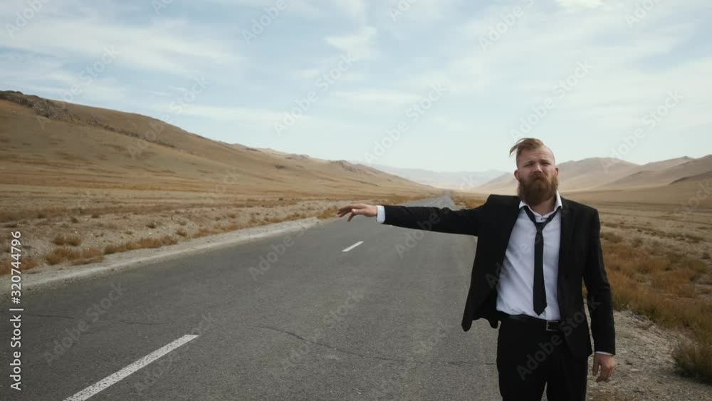 man with beard mustache black suit with tie in sneakers with white soles office worker stands on the road steppe, catches car, close-up, pensive, looks into the distance caucasian man with beard mustache black suit with tie in sneakers with white soles office worker stands on the road steppe, catches car, close-up, pensive, looks into the distance caucasian