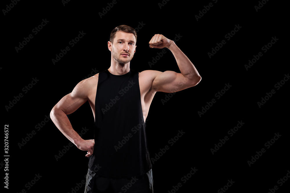 Young strong athlete in sportswear keeping one hand on waist while showing his strength in front of camera in isolation Young strong athlete in sportswear keeping one hand on waist while showing his strength in front of camera in isolation