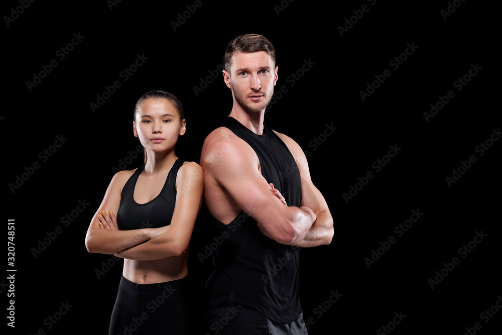 Young fit sportsman and sportswoman in black activewear standing close to one another with arms crossed by chest